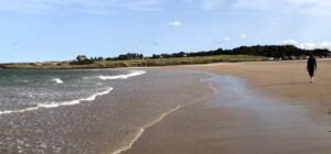 person walking along a beach with waves coming in